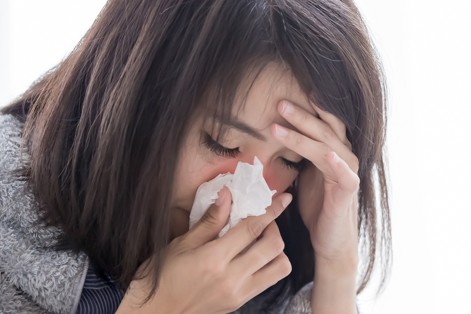 Allergies are Linked to Anxiety a stressed woman sneezing into a tissue