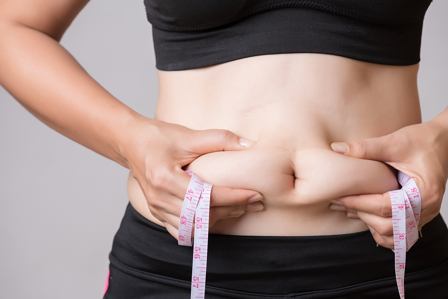4 Proven Ways to Release Belly Fat Faster a healthy woman squeezing her excess tummy fat
