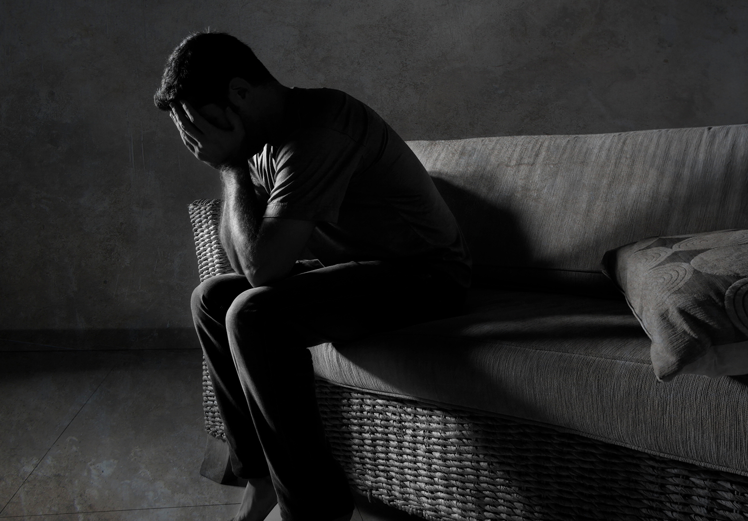 Bringing Suicide Into the Open A black and white portrait of young sad and depressed man sitting on a couch with his head in his hands