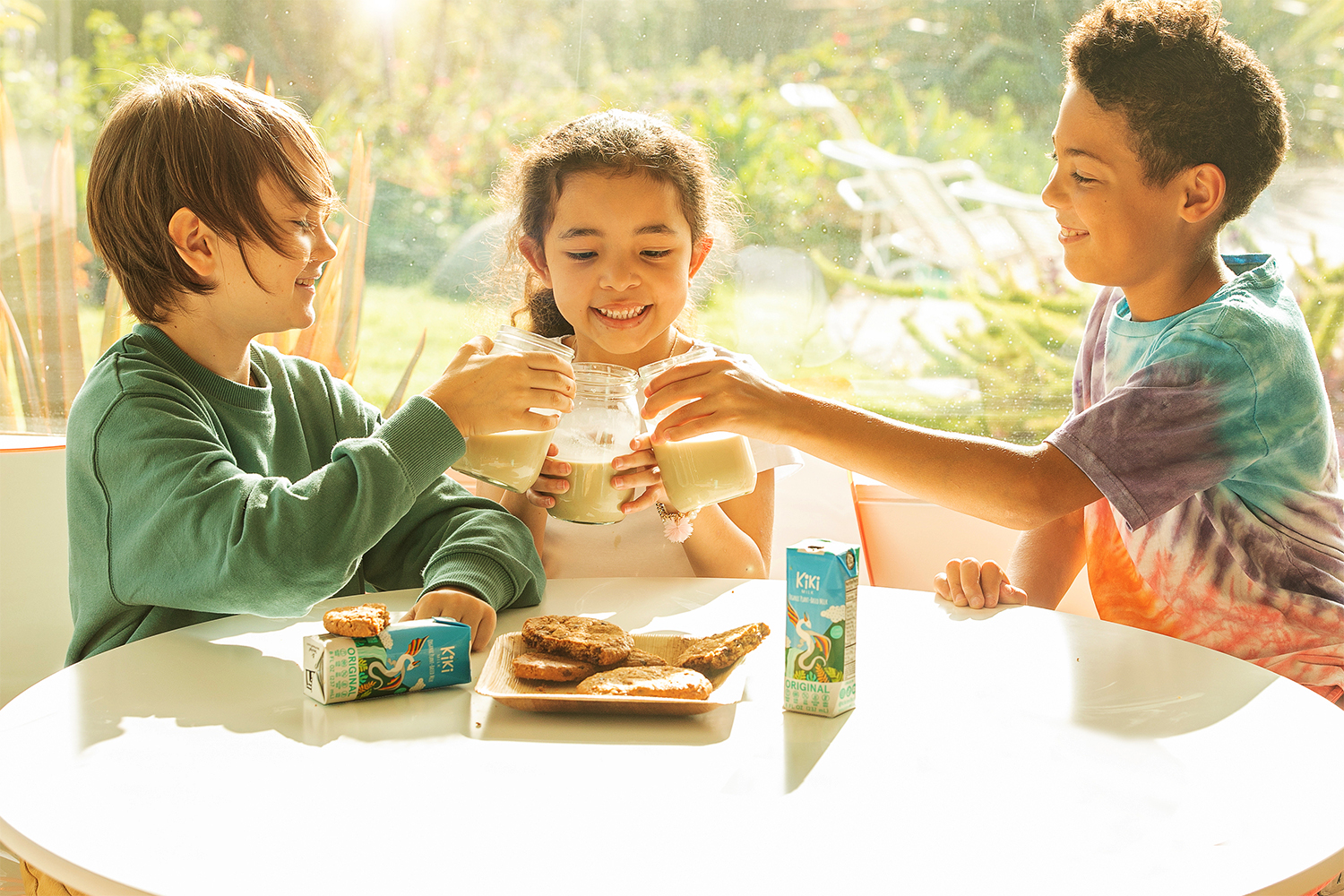 Kiki Milk kids sitting around a plate of cookies, cheering with glasses of plant-based milk