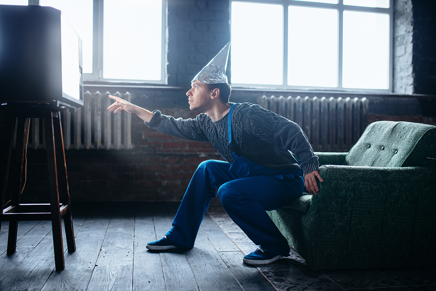 How the World Really Works a man in a tinfoil hat reaching to the glow of a television