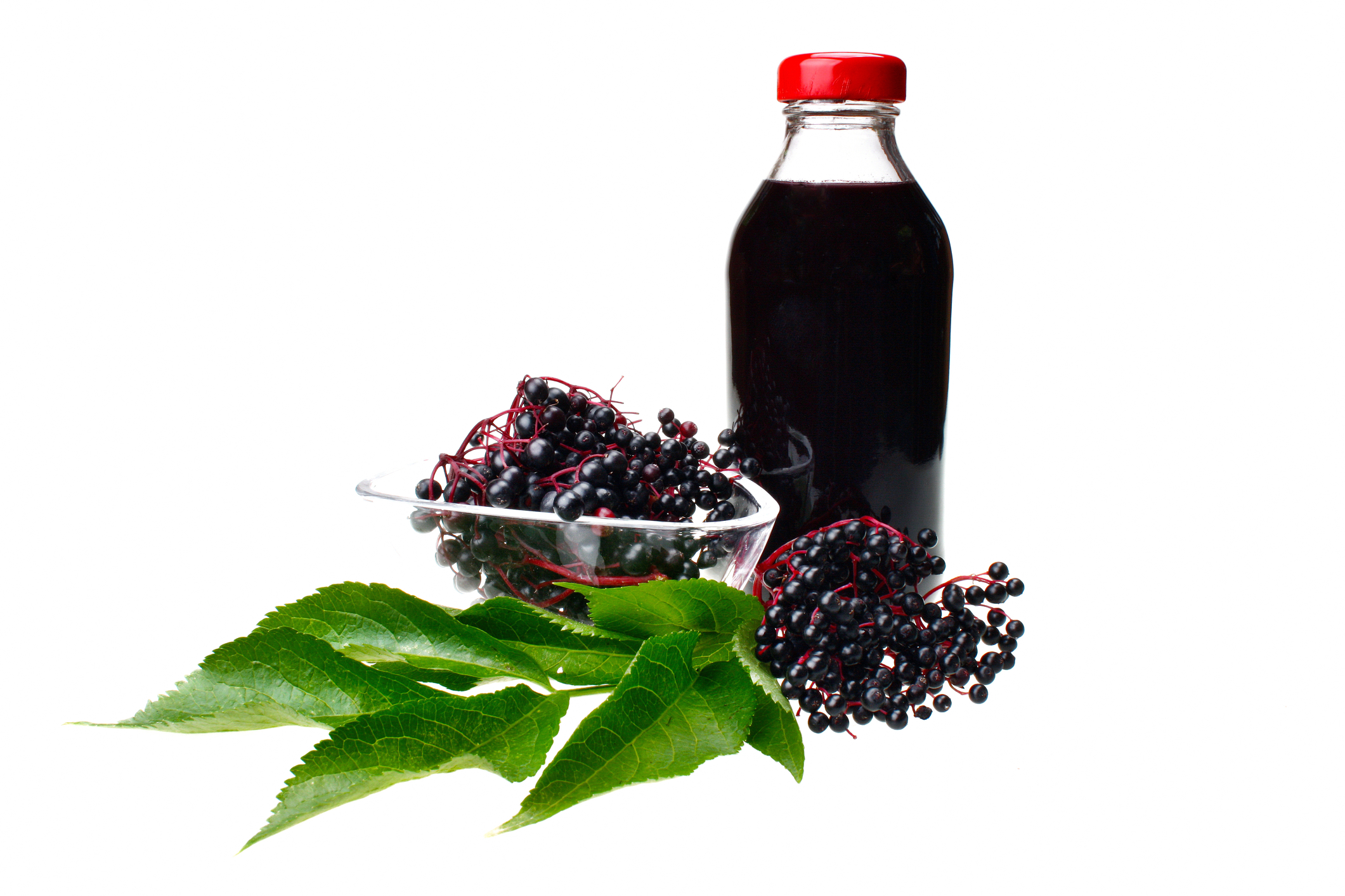 A glass jar of elderberry juice beside elderberry fruit bunches.