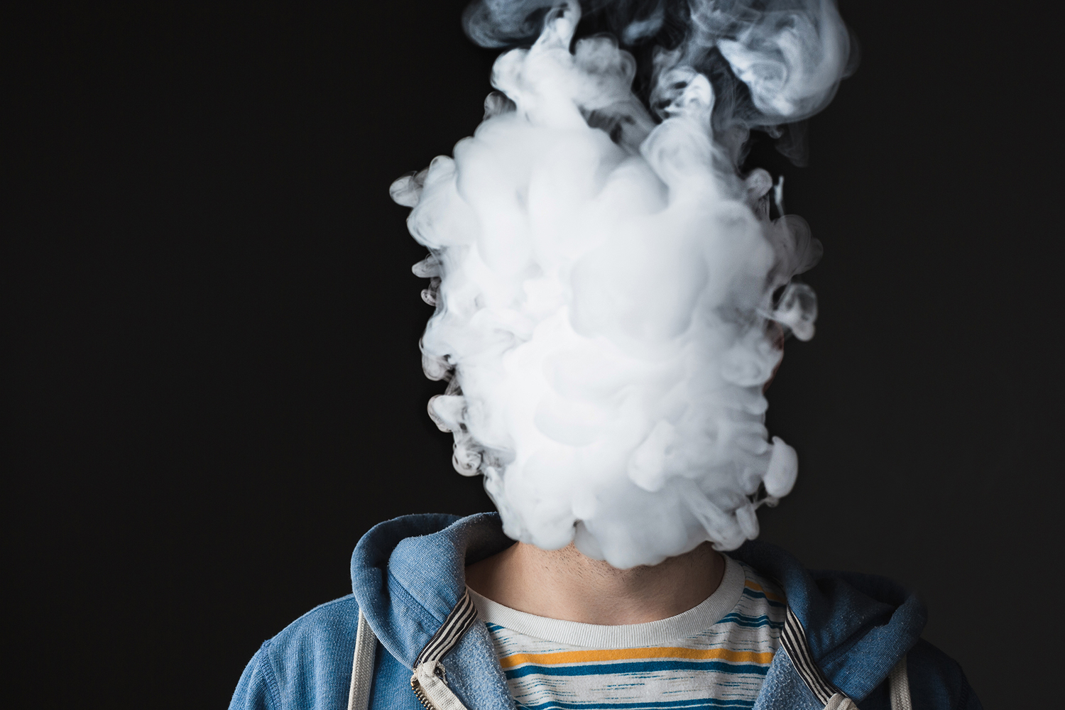 A young man with a plume of vapor covering his face.
