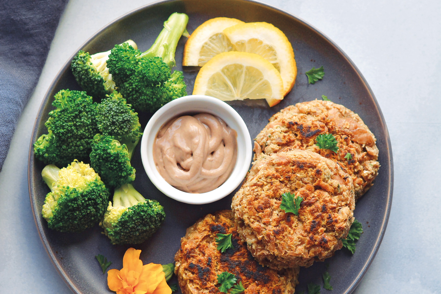 Hummus Tuna Cakes tuna cakes plated with hummus, broccoli, and lemon slices