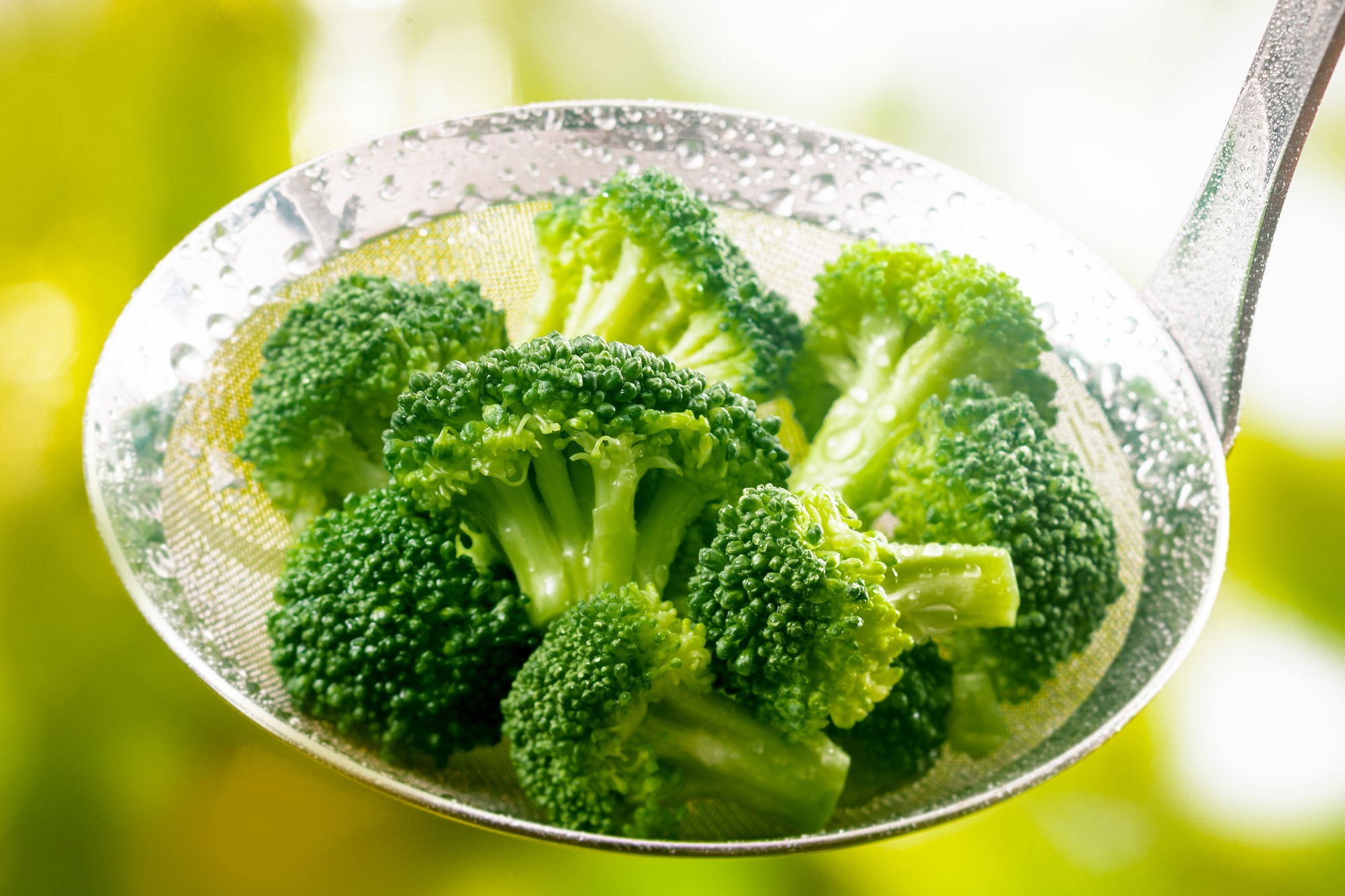 Steamed broccoli in a stainless steel ladle.