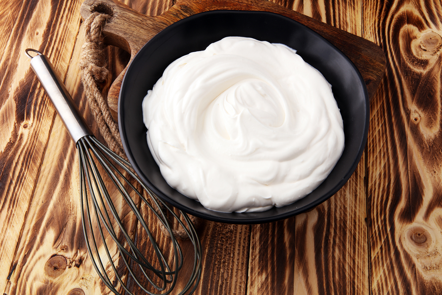Homemade Whipped Cream Homemade Whipped Cream in a black bowl with a whisk on a wooden table.