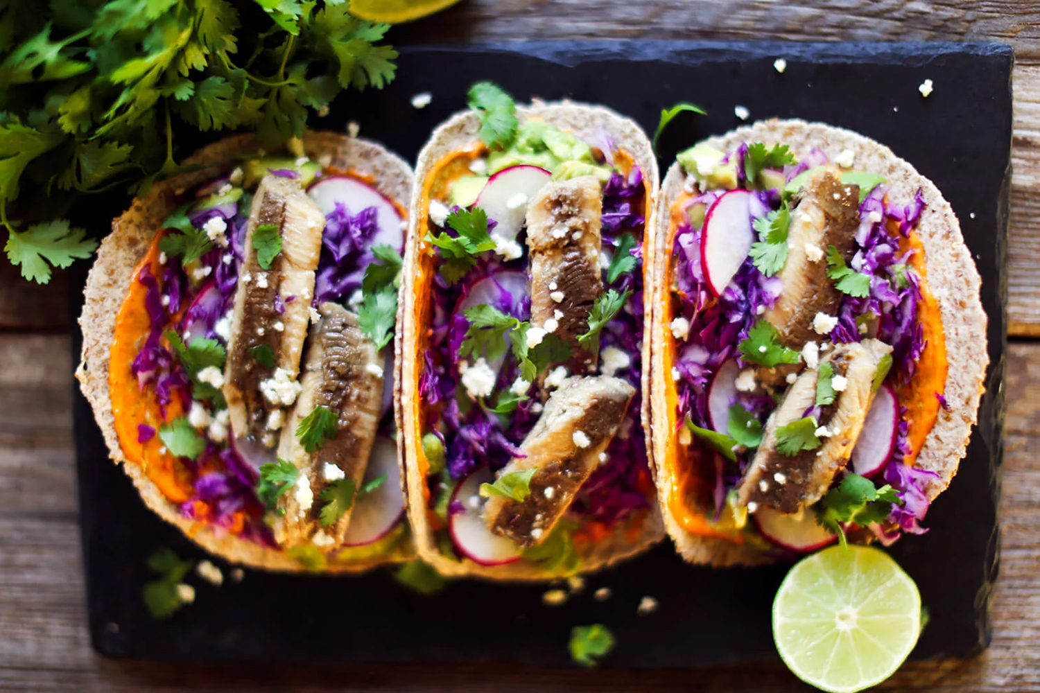 three sardine tacos served on a plate with lime