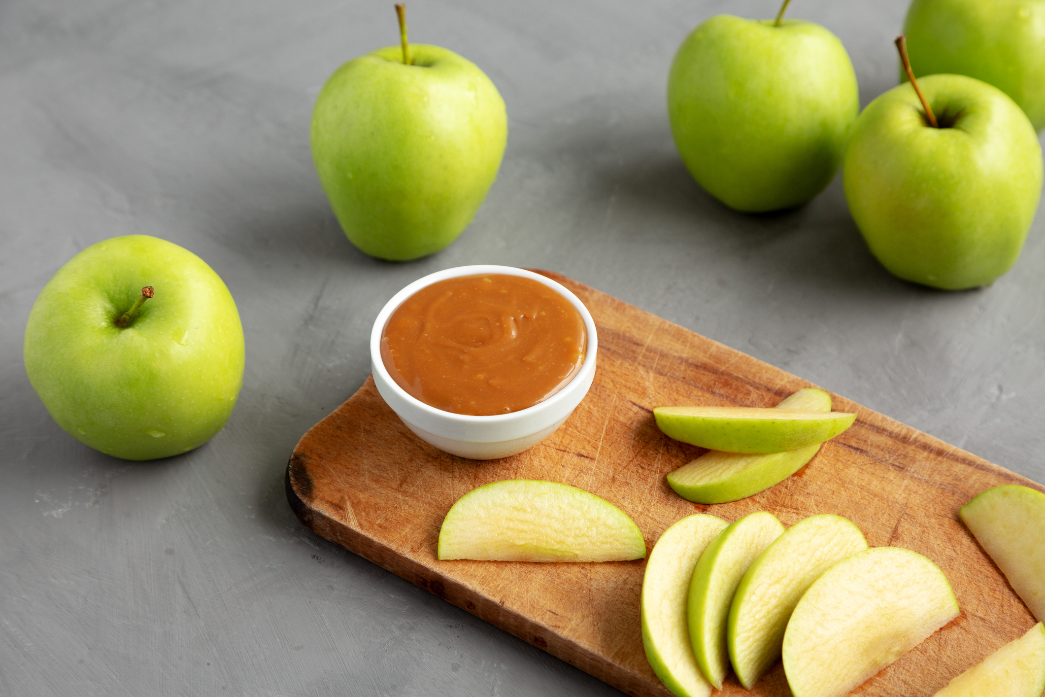 Raw Salted Caramel Apple Dip Caramel dip in a bowl on a cutting board with sliced green apples.