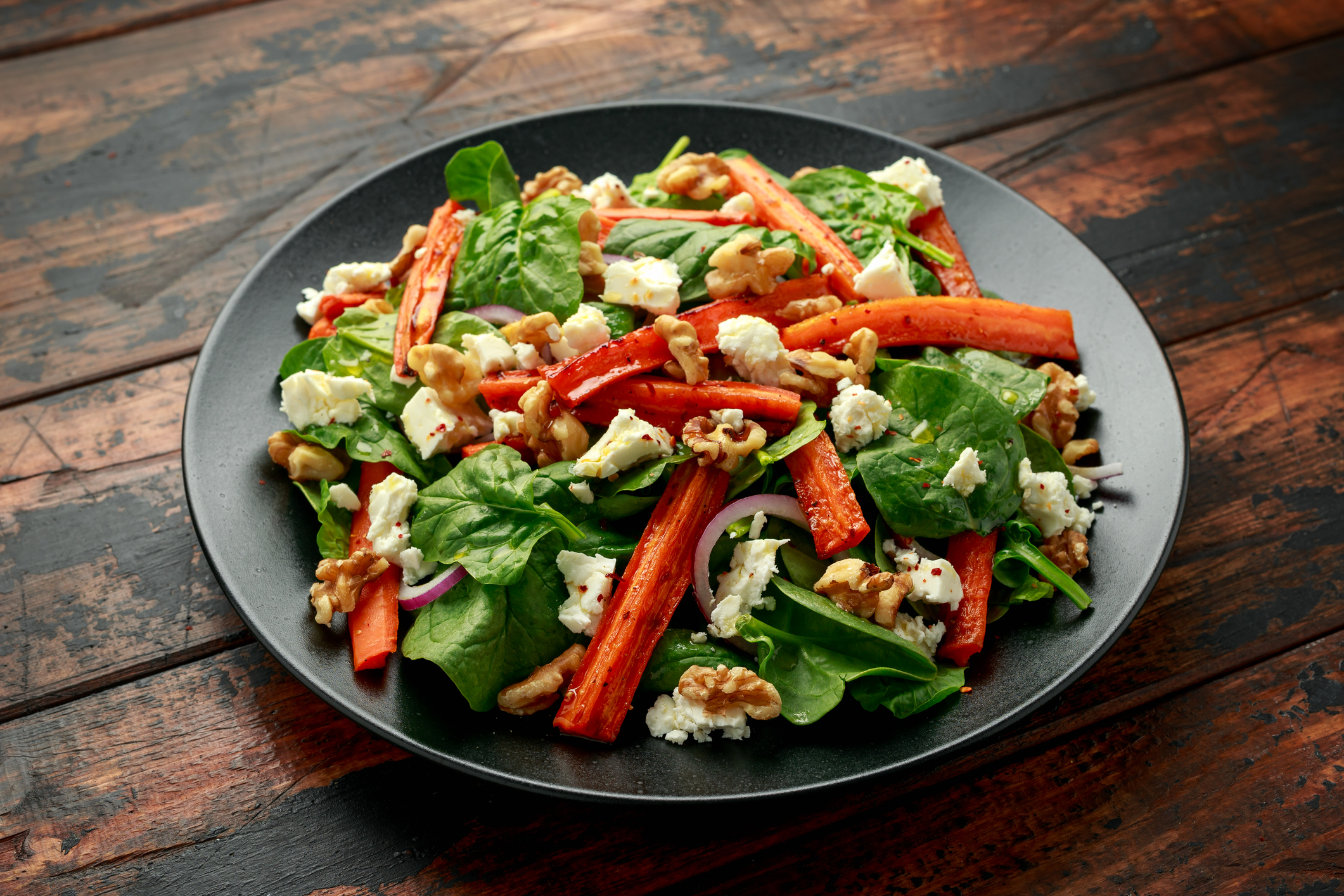 Grey salad plate filled with spinach, roasted carrots, cheese, and walnuts.