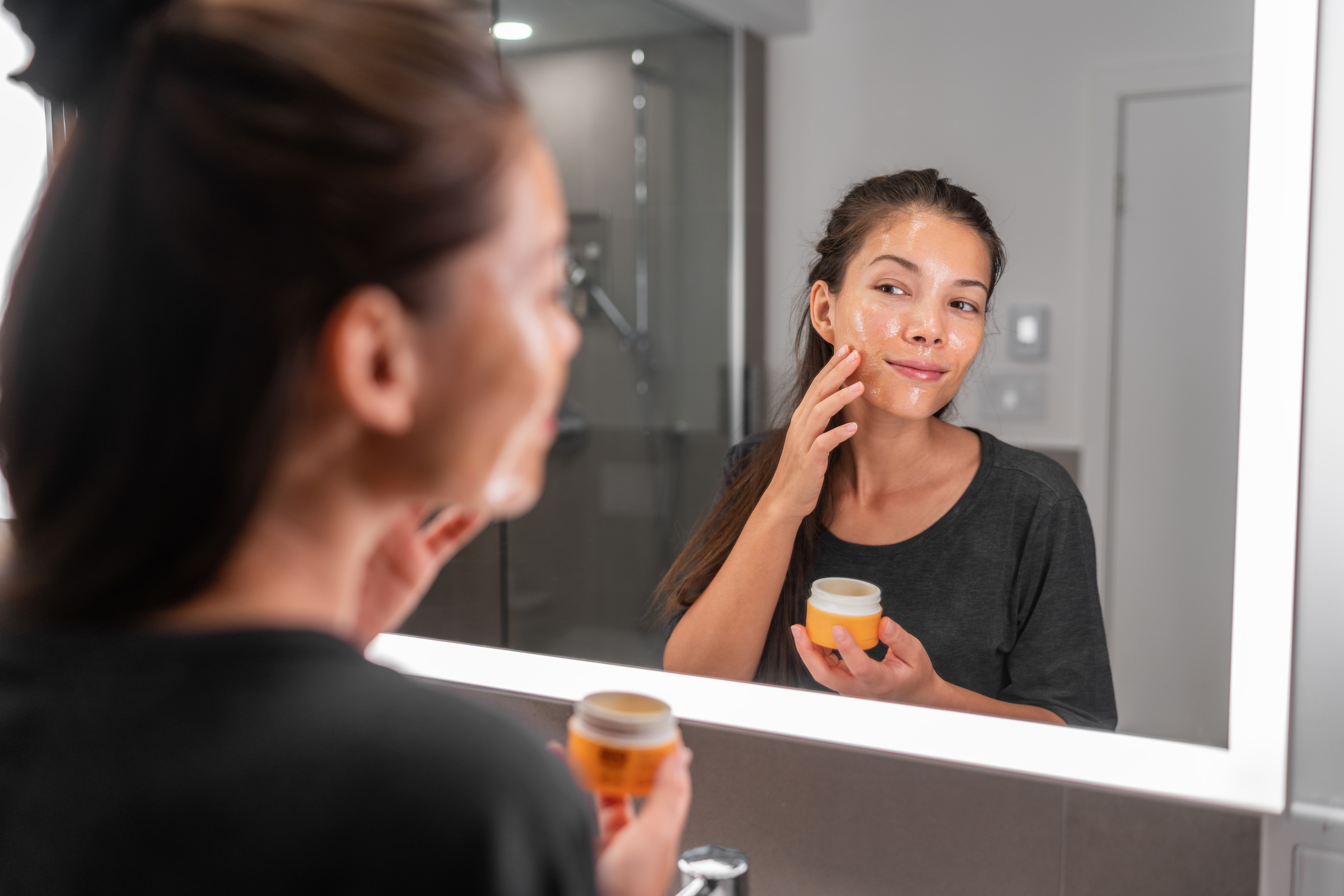Manuka Honey A woman adding honey to her skin in front of a bathroom mirror.