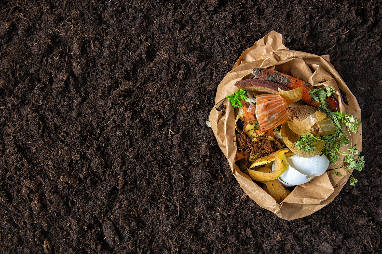 Top view of beautifully enriched soil with a bag of kitchen scraps to be composted.