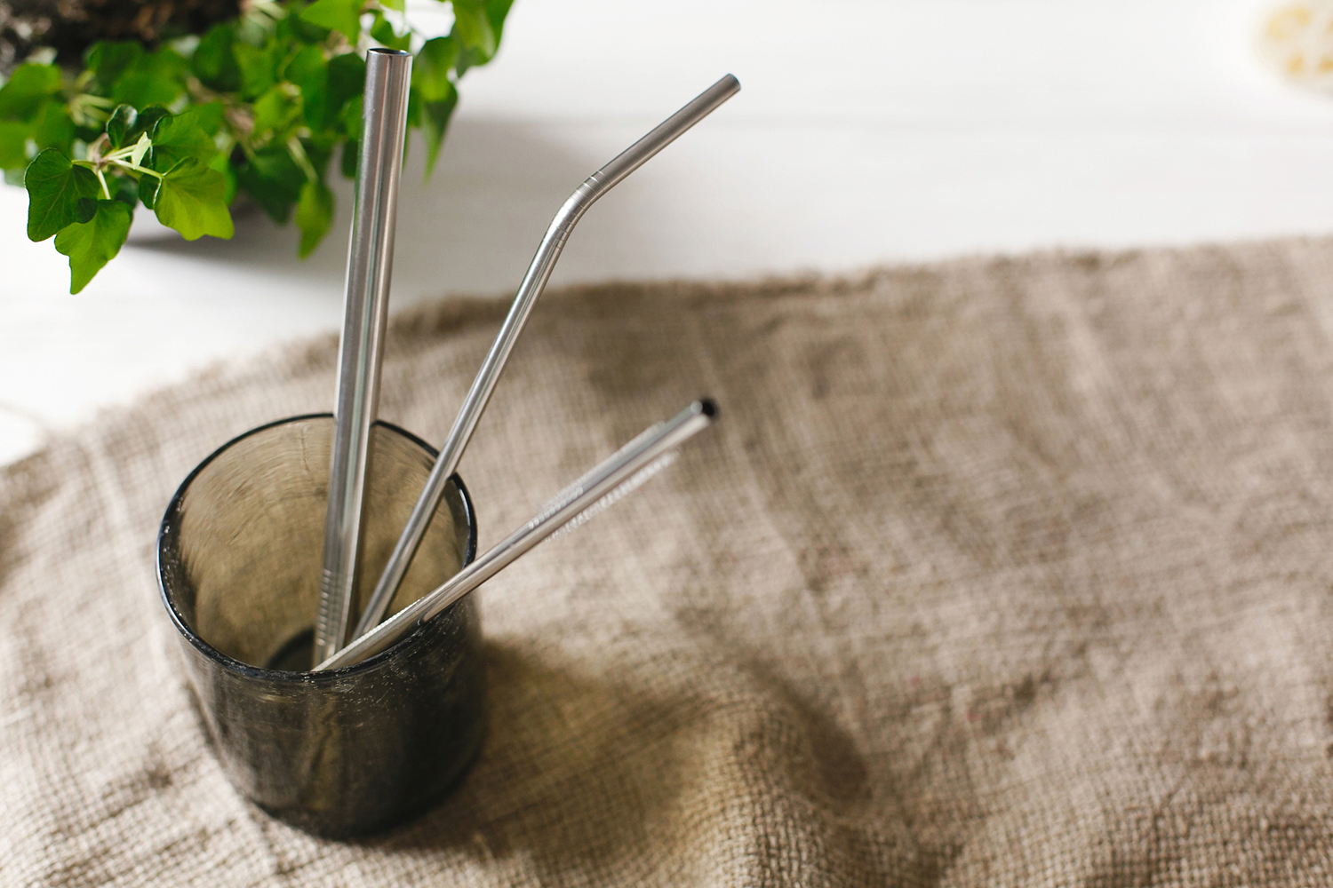 Eco natural metallic straws in green glass on rustic background with greenery.