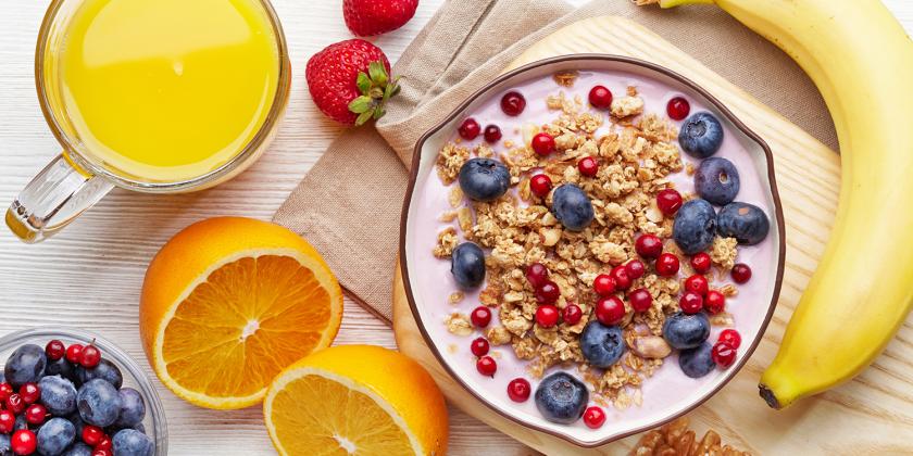 A bowl of granola, nuts, and yogurt with fresh fruits and juice