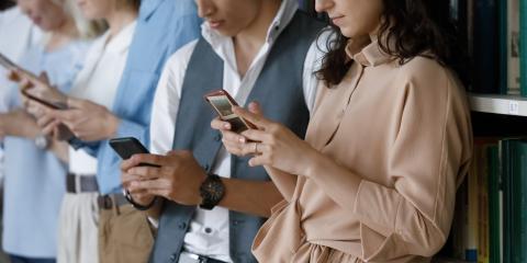 Line of people standing near book shelves, all looking at cell phones.