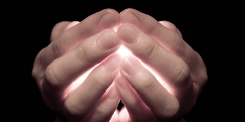 hands clasping a glowing light in the dark