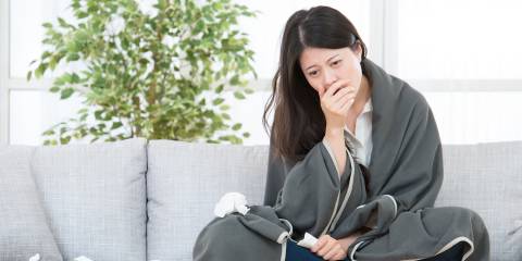 A woman on the couch with a blanket and a pile of tissues