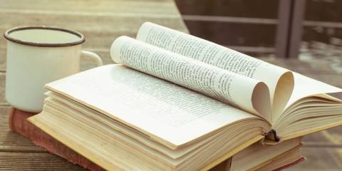 Opened vintage book on the wooden table with old fashioned cup of tea.