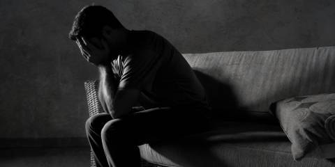 A black and white portrait of young sad and depressed man sitting on a couch with his head in his hands