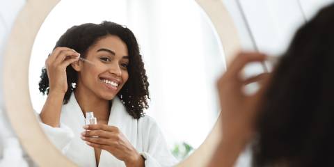a woman applying serum to her face in the mirror