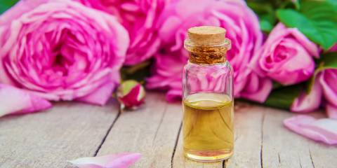 Avocado & Rose Face Oil Rose hip oil in a clear corked jar. Pink roses in the background.