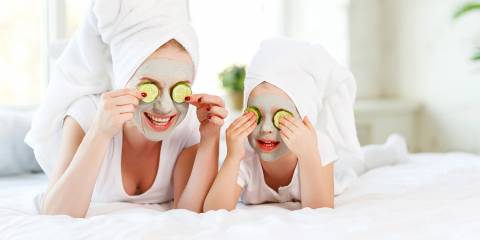 Mother and child with natural face masks on, covering eyes with cucumber slices.
