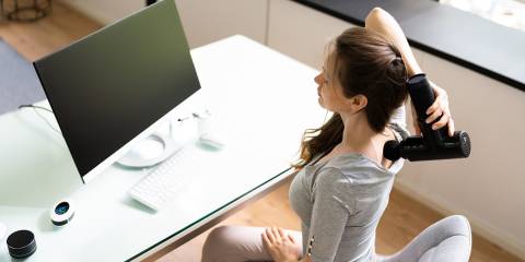 a woman using a massage gun on her neck, her back