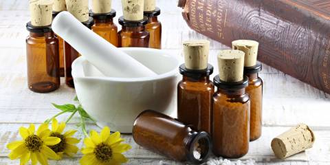 Arnica Tablets with arnica flowers next to an old Homeopathic medical book.