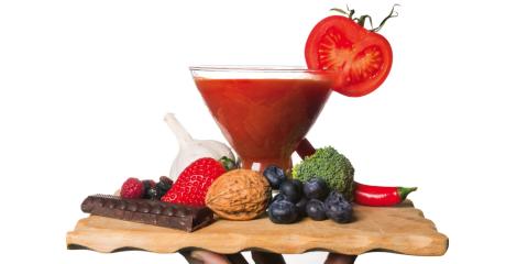 Hand holding dish of cancer fighting foods, including smoothie, tomatoes, broccoli and blueberries