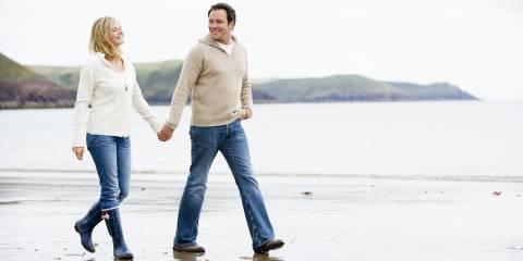a middle-aged couple holding hands while they walk down a rugged beach