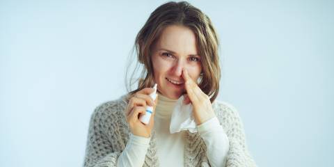 a middle-aged woman with tissues and nasal spray