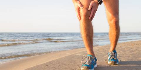 A man with an aching knee while running on the beach