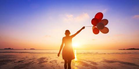 a happy woman holding balloons on the beach at sunset