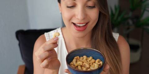a young woman smiling while eating raw cashews