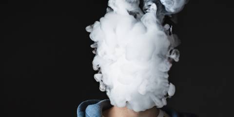 A young man with a plume of vapor covering his face.