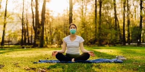 Mindful Living During the Pandemic a woman wearing a mask, meditating in a sunny park
