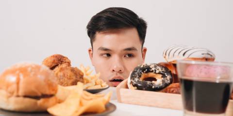 How to Outsmart Food Cravings Young man having cravings for donuts, hamburger, chicken with fries.