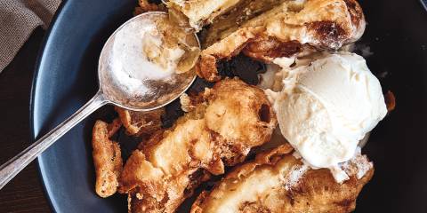 Banana fritters served in a blue bowl with vanilla ice cream.