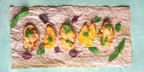 Crispy potatoes on parchment paper garnished with herbs and greens on a light blue background.
