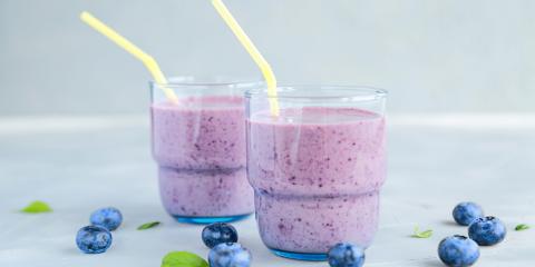 Two glasses of blueberry spinach smoothies, each with a pale yellow straw. 