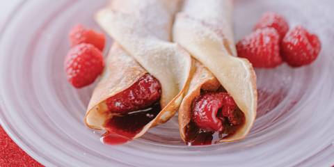 Jam Crêpes with Vanilla Sugar on a white swirled glass plate garnished with raspberries.