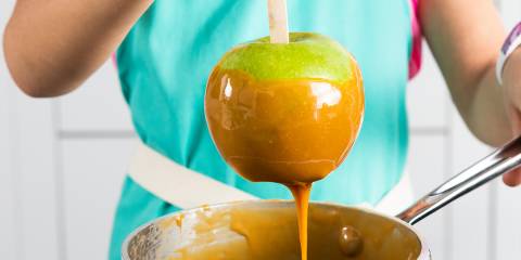 Caramel Apples A woman dipping a Granny Smith apple in a pot of caramel to make caramel apples.