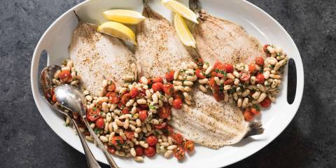 Roasted Trout with White Bean and Tomato Salad  A top view of Roasted Trout with White Bean and Tomato Salad on a white serving tray with a charcoal gray background.