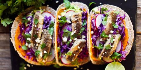 three sardine tacos served on a plate with lime