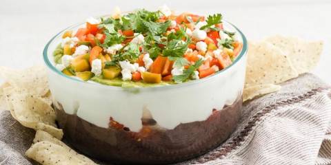 A bowl of seven-layer bean dip surrounded by tortilla chips