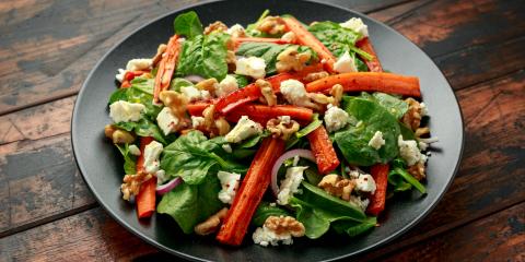 Grey salad plate filled with spinach, roasted carrots, cheese, and walnuts.