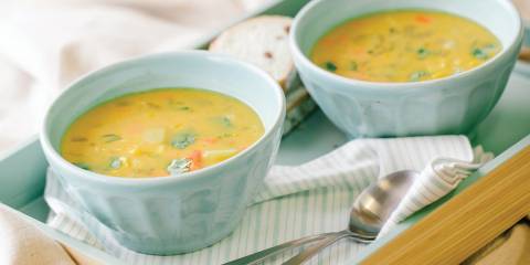 Two light blue bowls of coconut corn chowder on a bamboo serving tray.