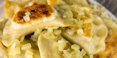 a plate piled with fresh pierogi topped with saurkraut