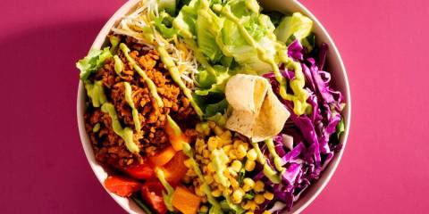 a bowl of lettuce, corn, peppers, and vegan taco filling