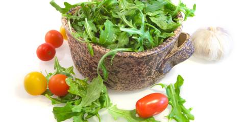 Arugula Salad with Tomato Vinaigrette Bowl of arugula with cherry tomatoes and a bulb of garlic surrounding the bowl