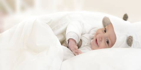 A happy baby smiling snuggled in a white blanket